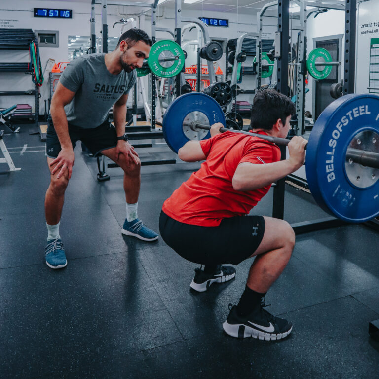 Image of a Saltus Performance coaching an athlete on his squats
